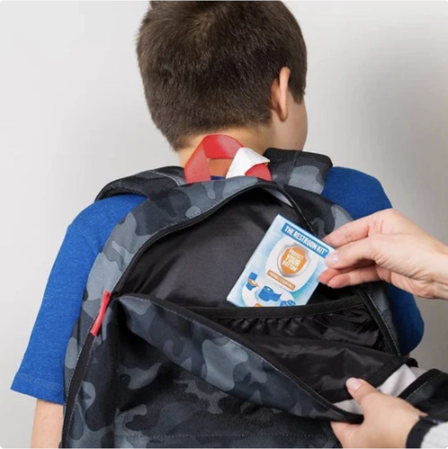 A parent slipping a sealed Restroom Kit into a child's school backpack